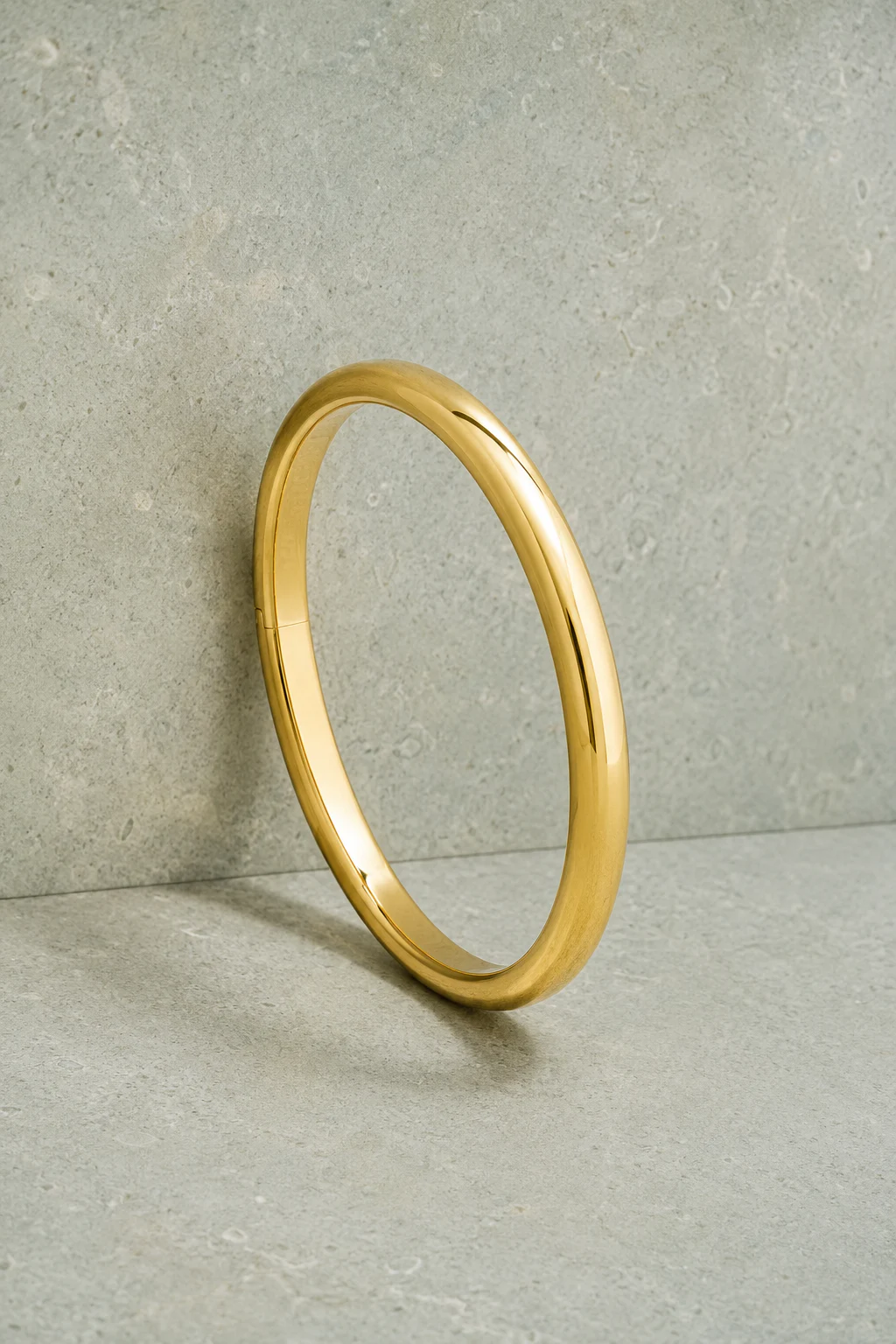 Classic yellow-gold hinged bangle on a neutral architectural surface